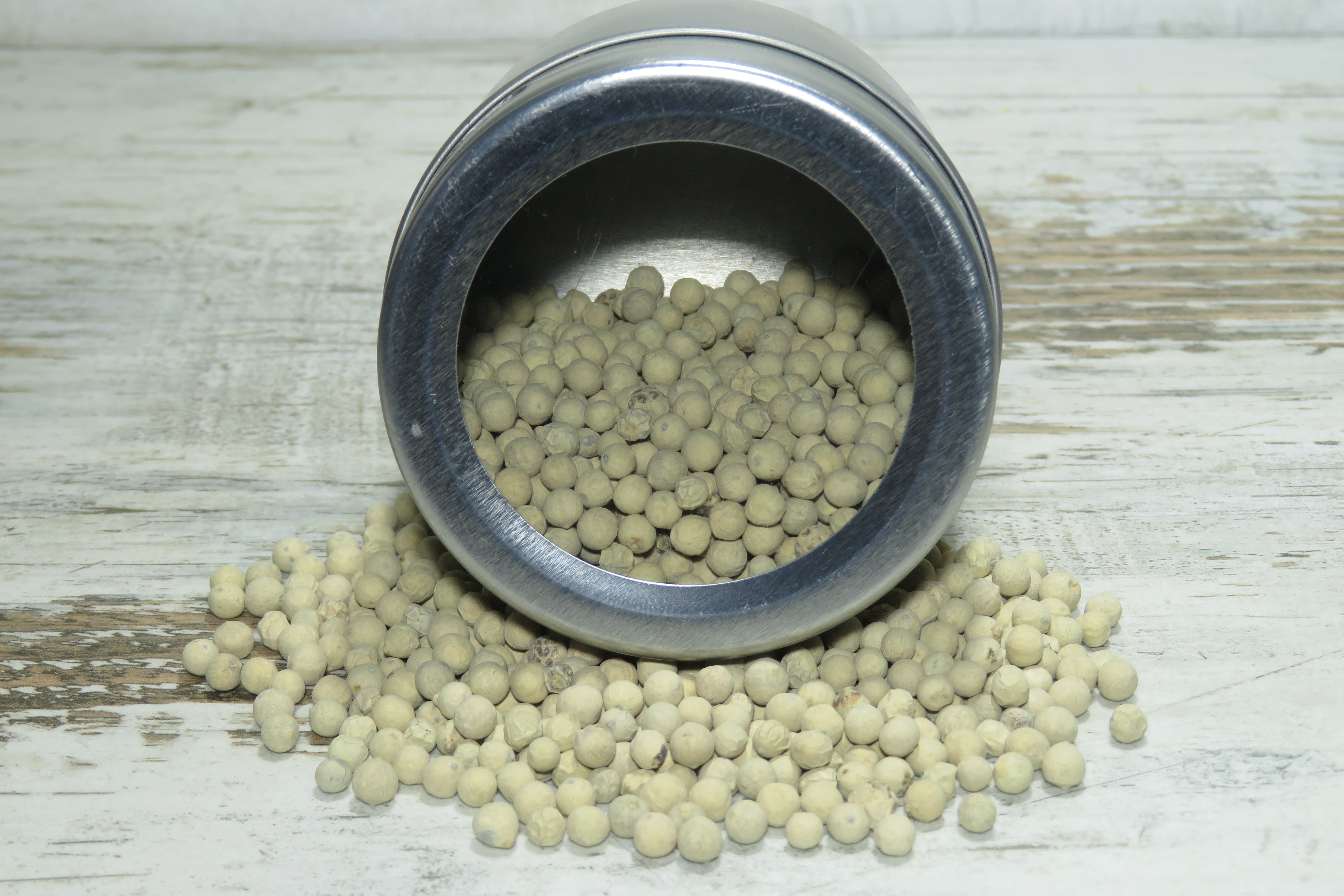 Nahaufnahme einer Streudose mit weissem Pfeffer aus Sansibar, umgeben von Pfefferkörnern.