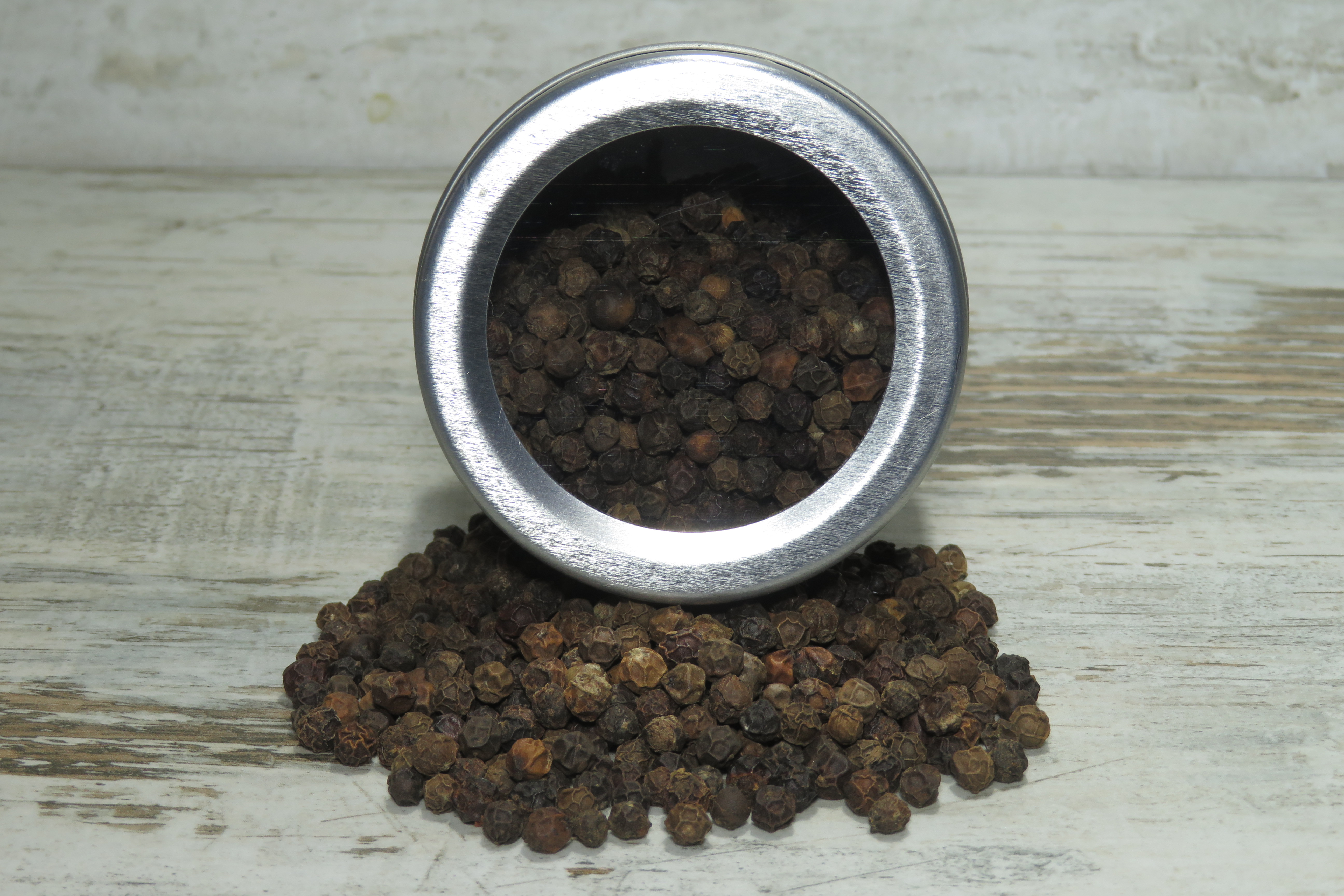 Nahaufnahme einer Streudose mit schwarzem Pfeffer aus Sansibar, umgeben von Pfefferkörnern.